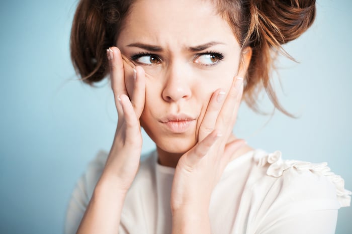 A female model holds her face and makes a tense face looking to the side of camera.