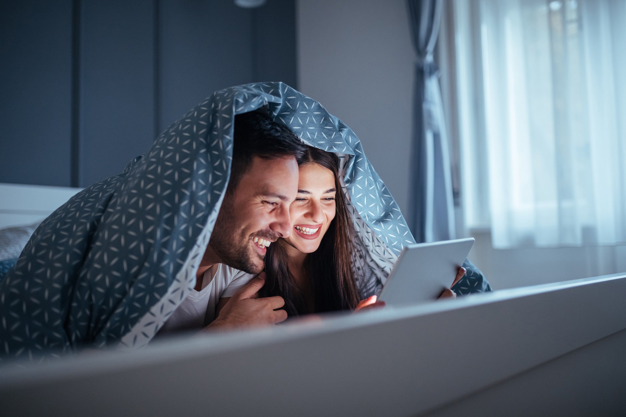 Smiling couple watching tablet in bed