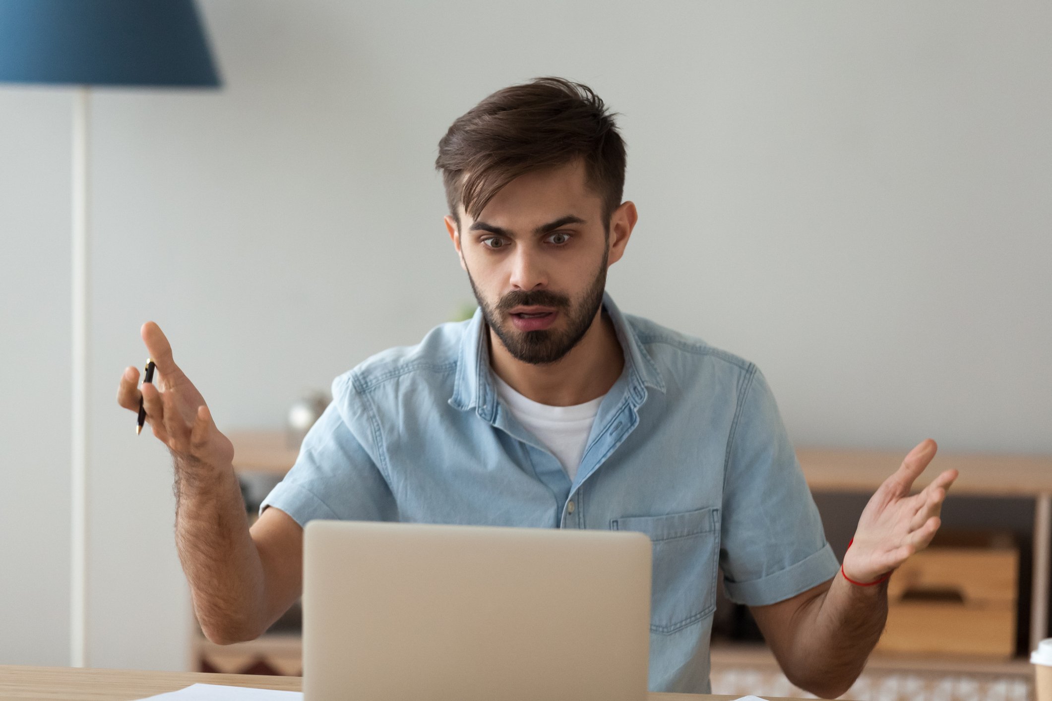 Wide-eyed office worker shrugs at his laptop.