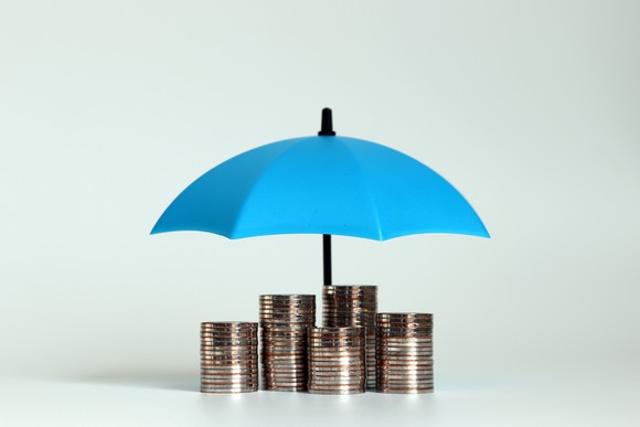 Miniature blue umbrella over piles of coins.