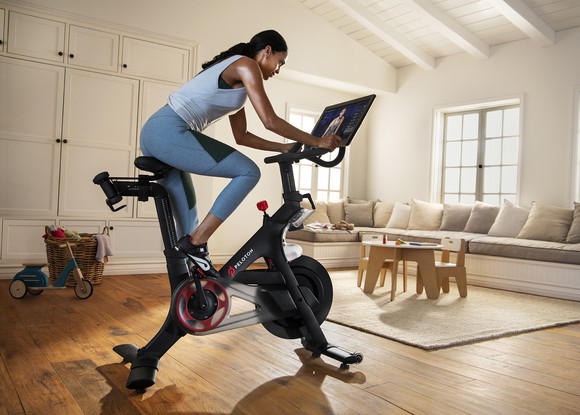 Woman riding a Peloton stationary bike in a living room.