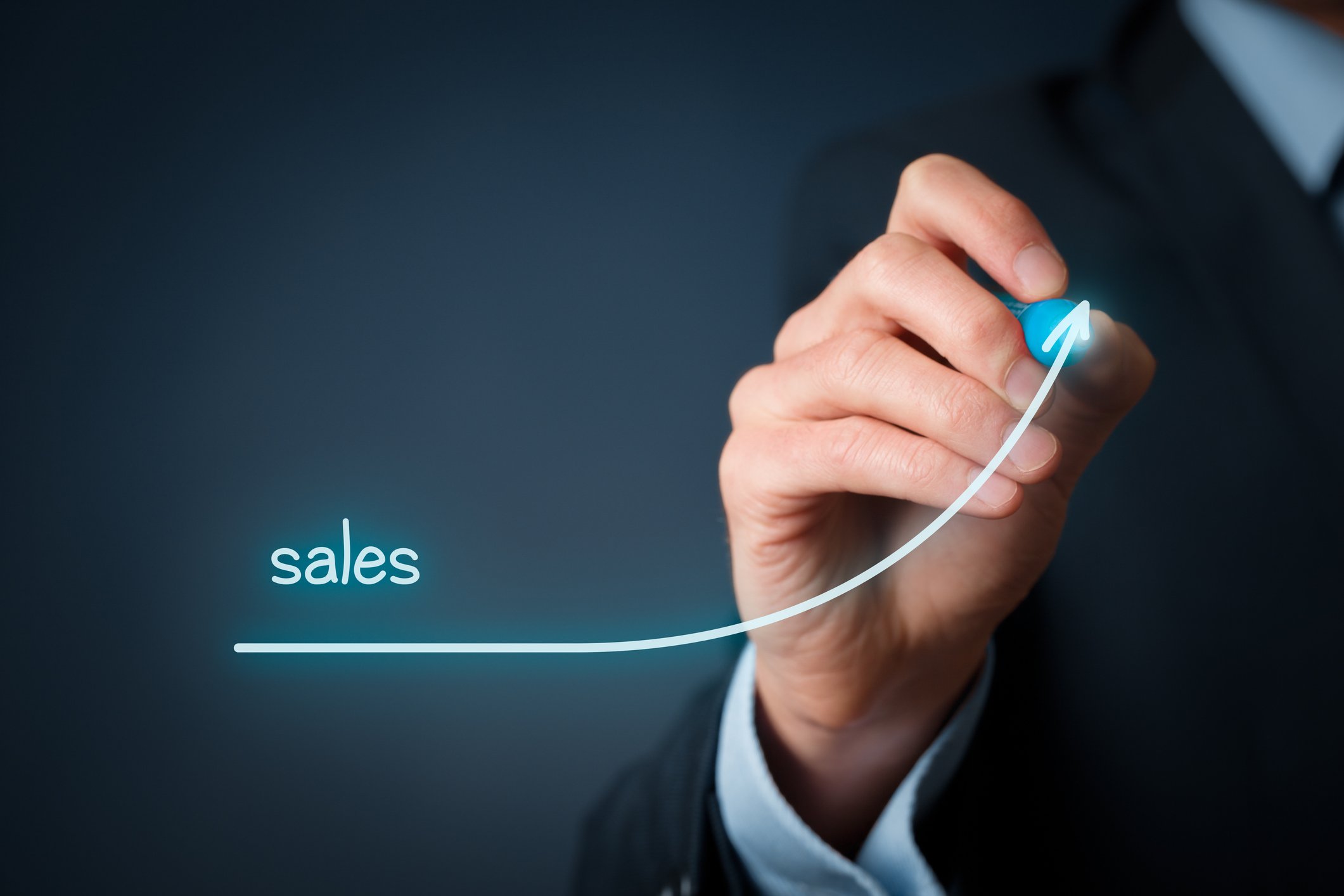 A person in a suit drawing an upward trending arrow with the word sales written above it.