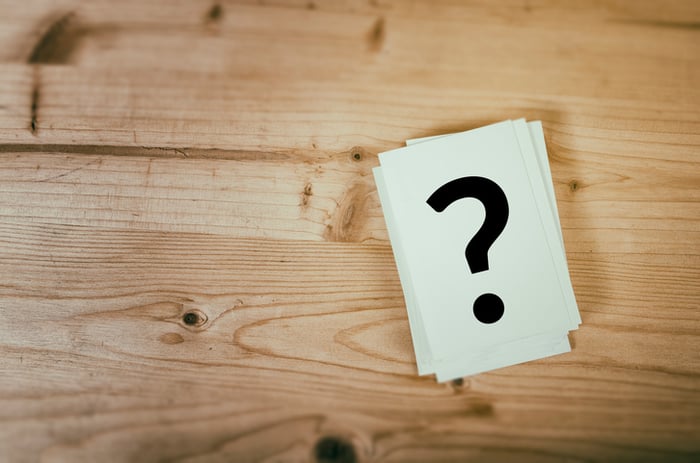 A question mark drawn on a card sitting on a wooden table.
