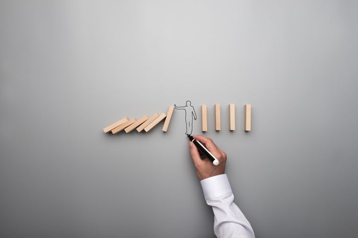 A hand drawing a stick figure holding up falling dominoes.