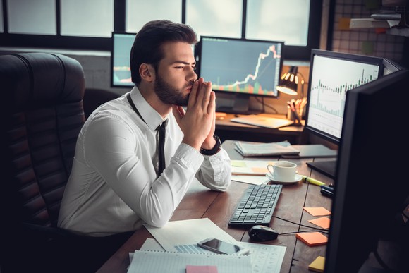 A young financial professional looks at his computer screens and weighs a decision. 
