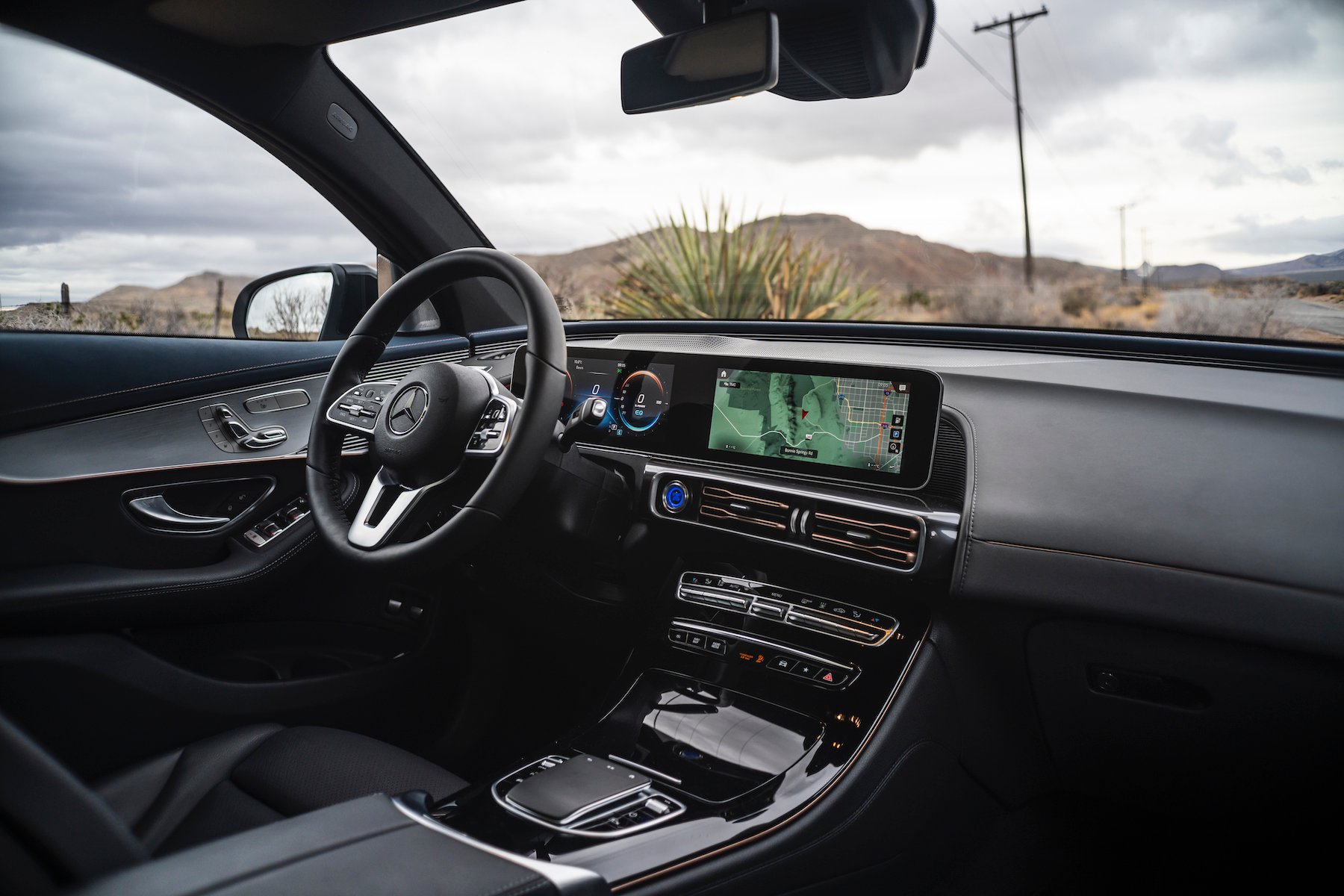 A view of the front seat and dashboard of a Mercedes-Benz EQC, showing a long touchscreen like the concepts with Mercedes' usual chrome-and-leather trim.