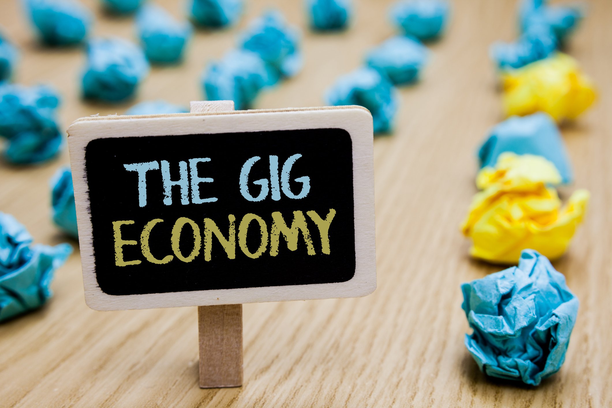 A sign displaying "The Gig Economy" with pieces of crumpled paper in the background.