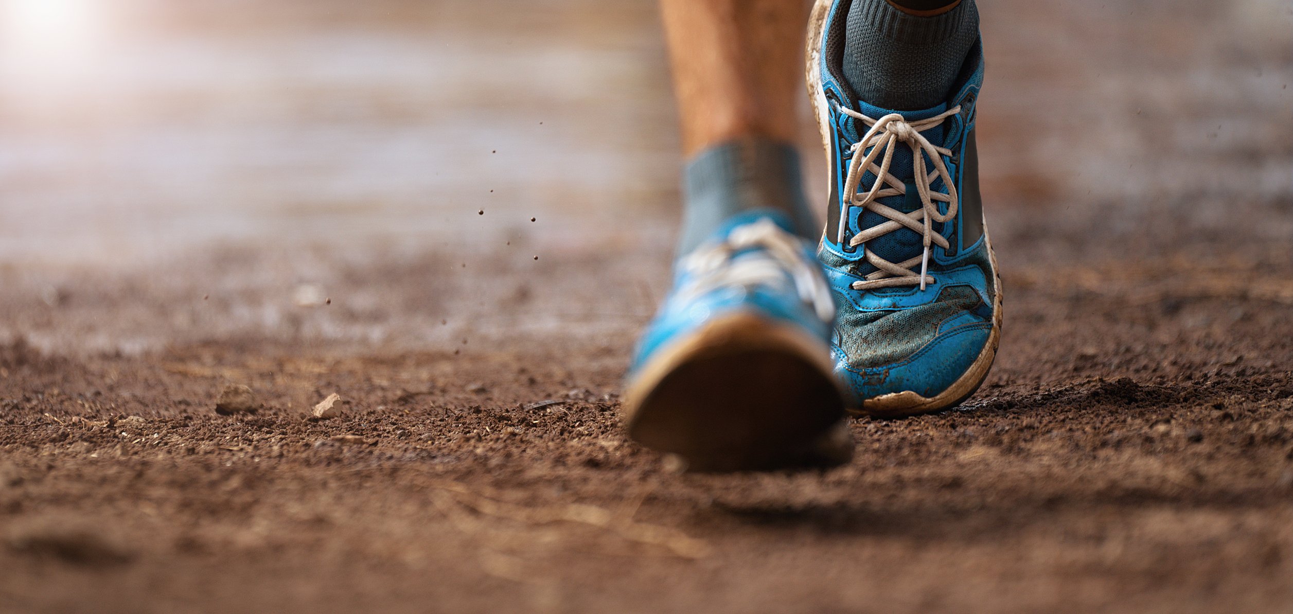 Close-up of two feet in athletic shoes walking an outdoor trail.