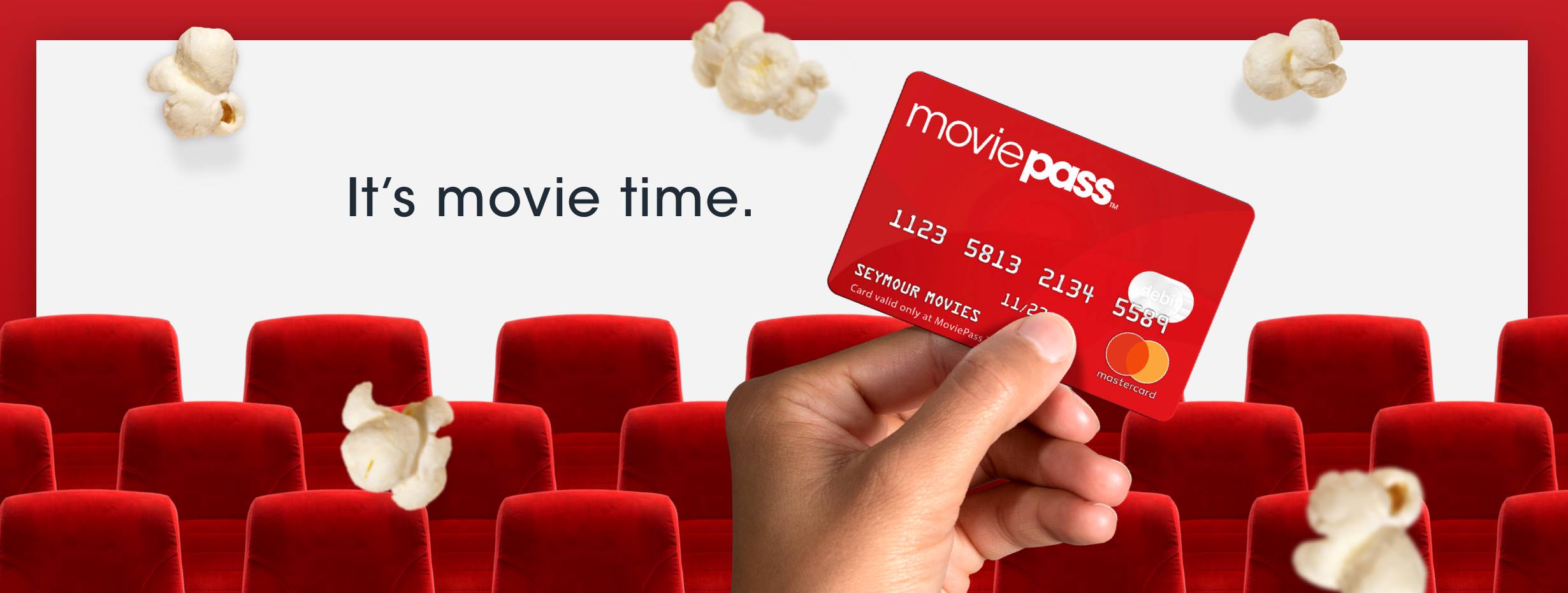 A MoviePass card being held up against falling popcorn in a movie theater.