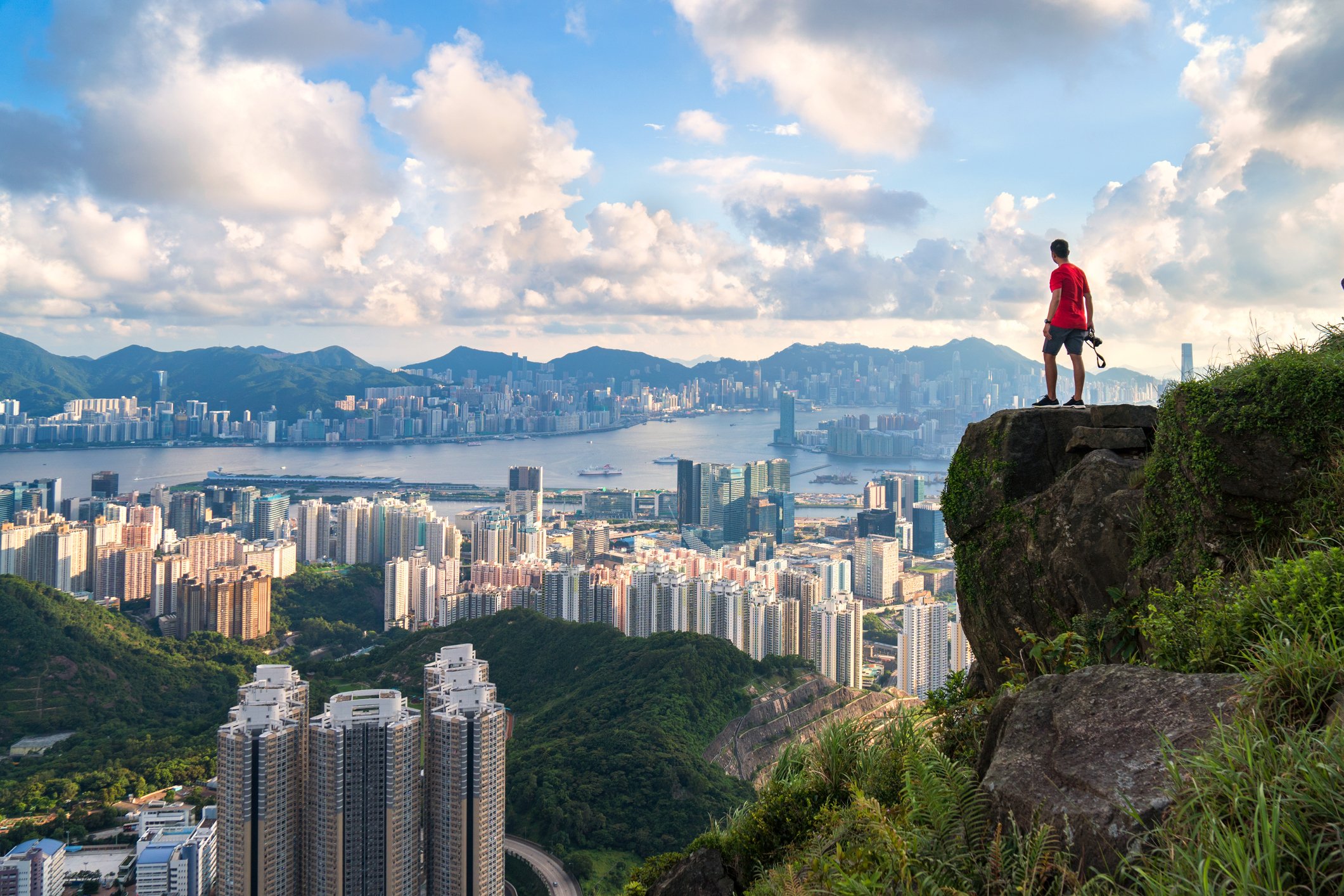 photographer standing on the top of Cliff above Hong kong cityscape.