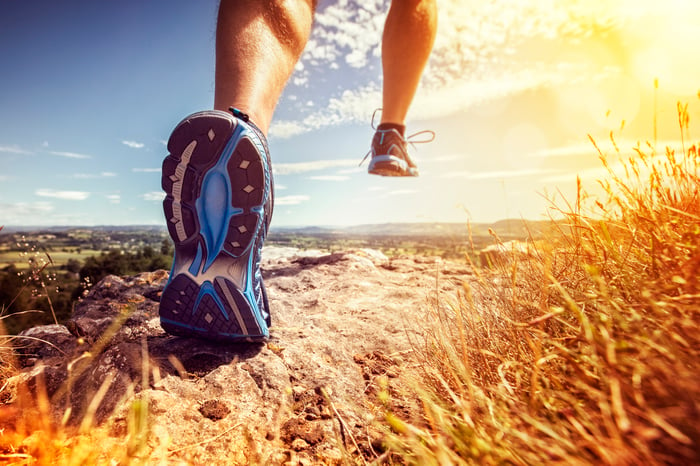 A jogger runs a trail with a wide valley vista ahead.