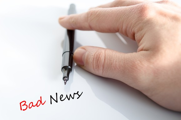 The words bad news written on paper, next to a hand and a pen.