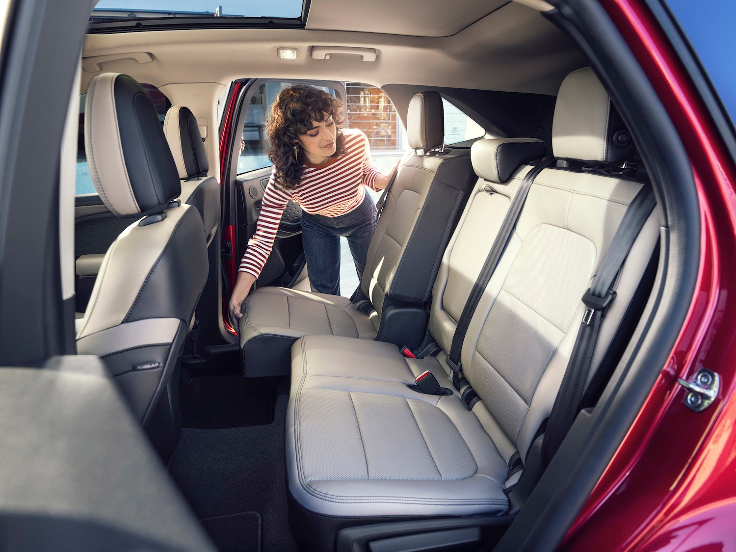 A woman moving the backseat of a red 2020 Ford Escape.