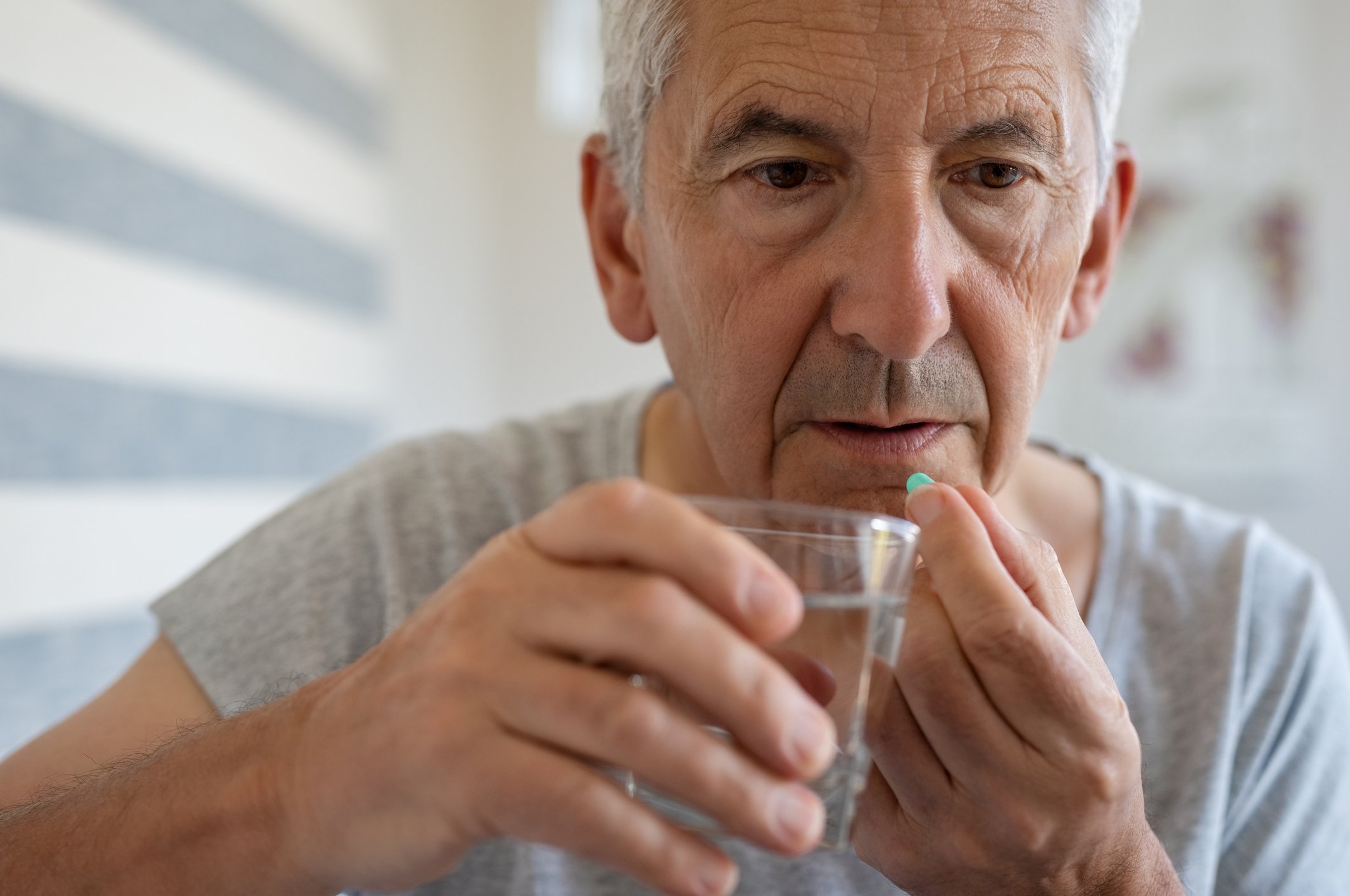 Older man taking a pill while holding a glass of water.