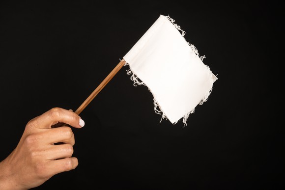 Hand holding a frayed white flag.