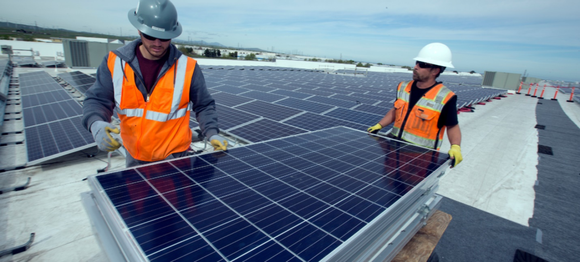 Workers installing solar panels on the roof of an Amazon warehouse