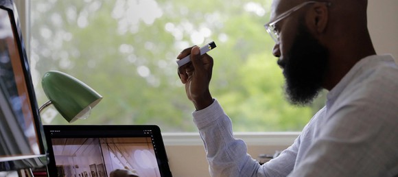 A man holds a Juul e-cigarette as he works in front of a laptop.