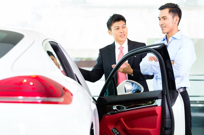 Two Asian men stand next to a car talking to each other