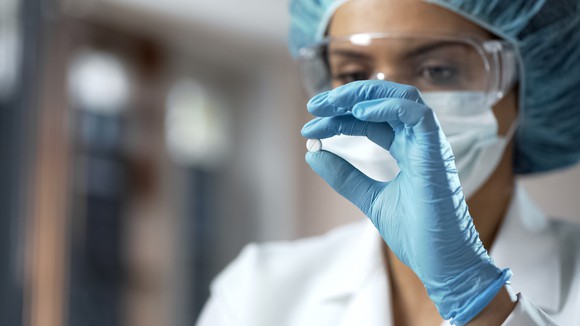 A female chemist inspecting a small white pill.