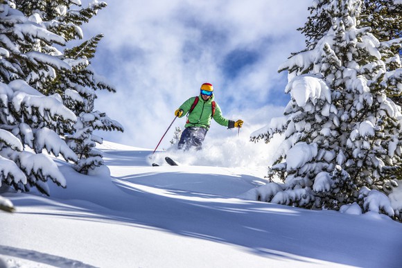 A man skiing down a mountain slope between snow-covered fir trees.