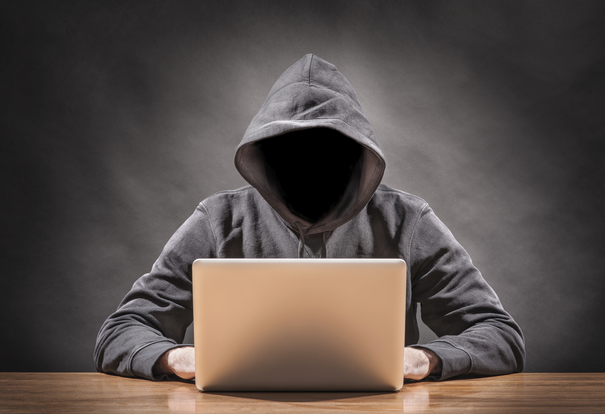 A faceless figure in a sweatshirt on a laptop computer, illustrating a hacker.