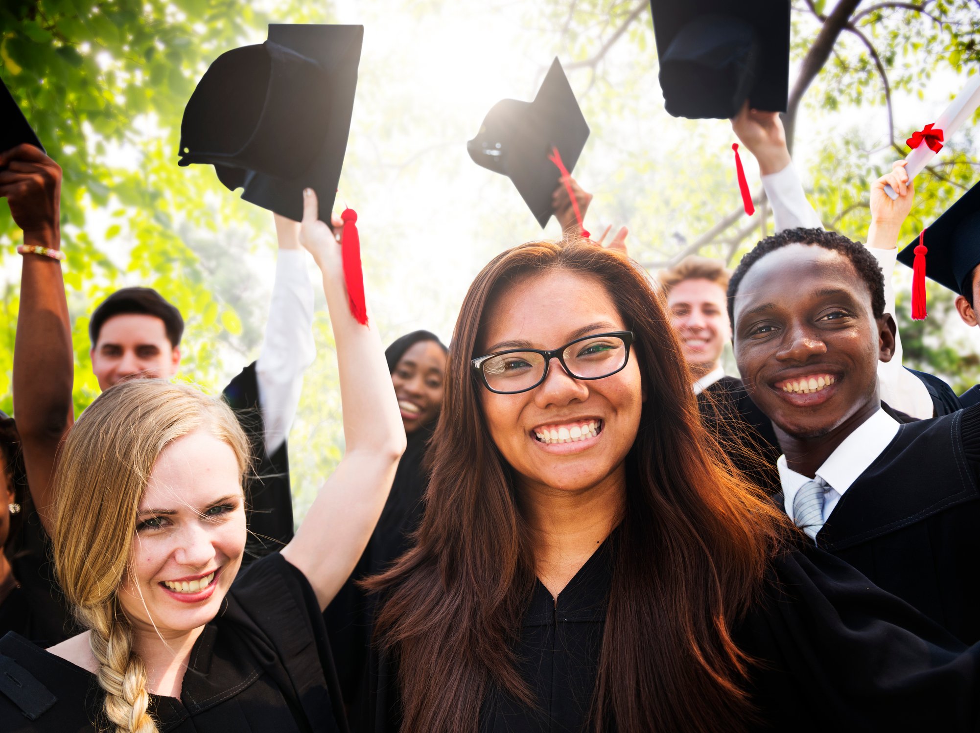 Smiling young adults in graduation gowns waving caps in the air