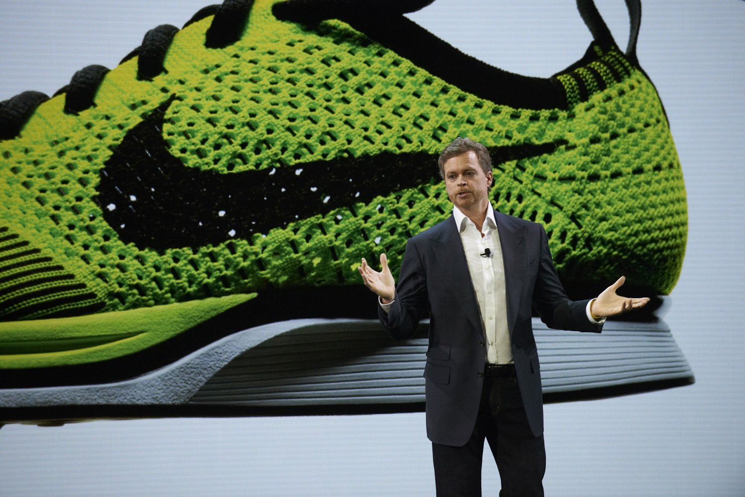 Nike CEO Mark Parker on stage in front of a large neon yellow Nike shoe.