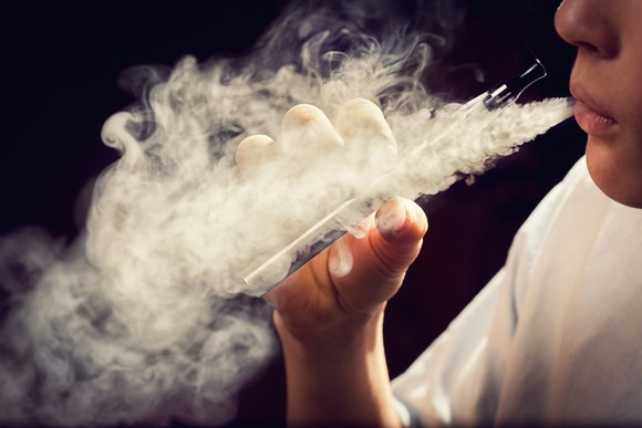 A person exhaling vape while holding an e-cigarette.