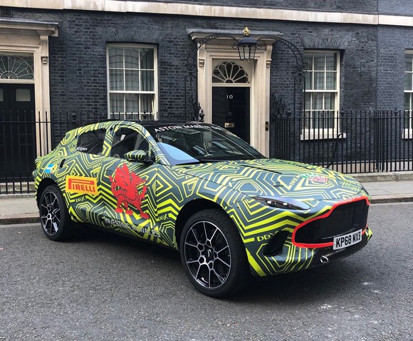 A prototype of the Aston Martin DBX, a luxury SUV, shown wrapped in green and yellow camouflage. 