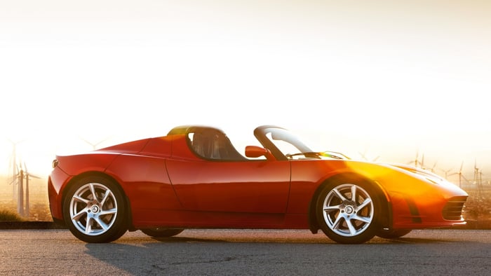 Tesla roadster in red on a road with bright sky and desert landscape behind.