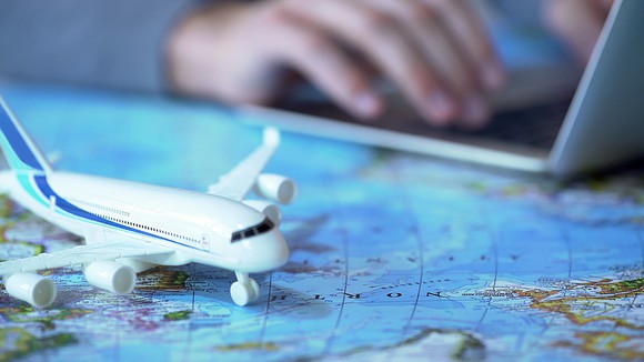 A model airplane on a world map, with a person booking tickets online in the background.