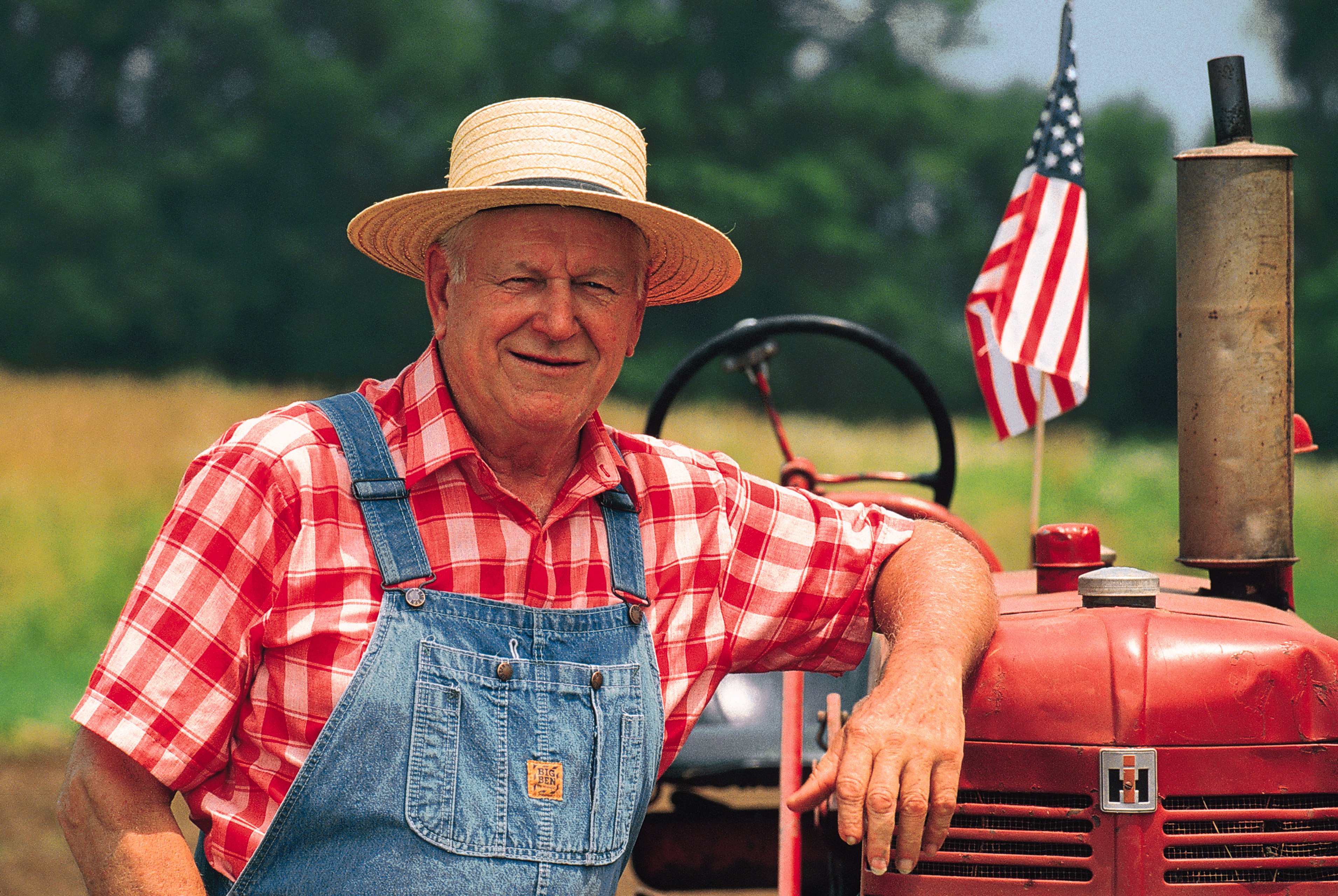 Farmer leaning on tractor with American flag on it.