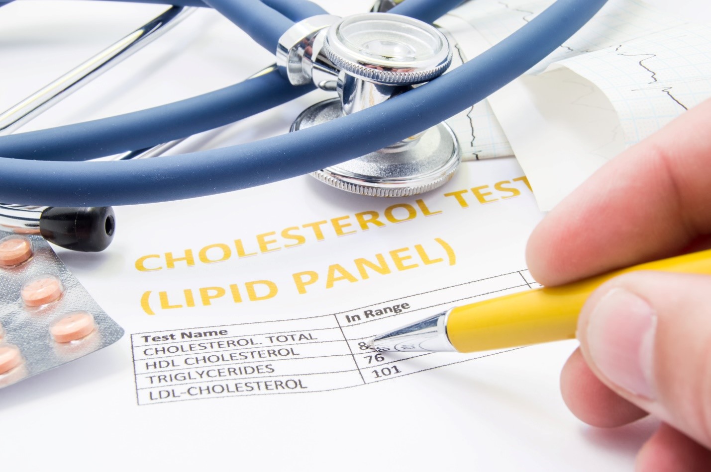 Cholesterol test results displayed on a sheet of paper alongside a stethoscope and some pills. 