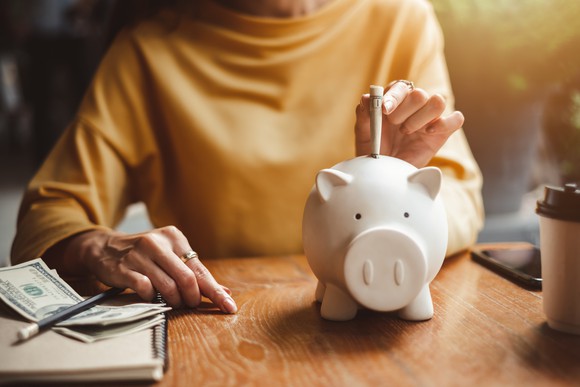 A woman putting cash into a piggy bank.