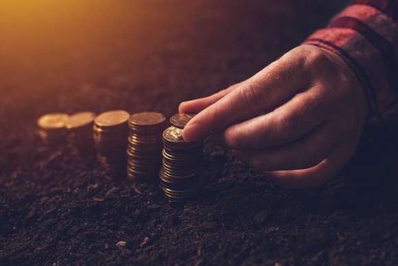 Stacks of coins in dirt and a hand placing a coin on one of the stacks.