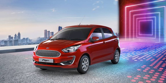 A red Ford Figo hatchback parked in front of a city skyline