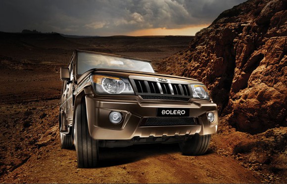 A brown Mahindra Bolero drives up a mountainous dirt road.