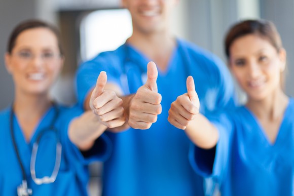Three people in blue scrubs giving a thumbs-up.