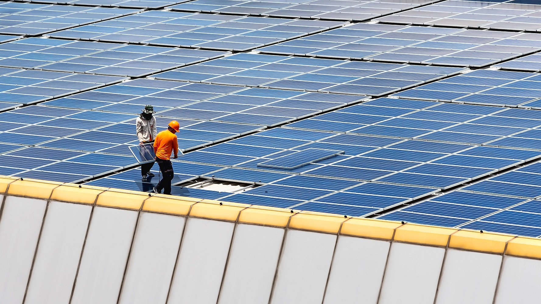 Workers installing a final solar panel on a large rooftop