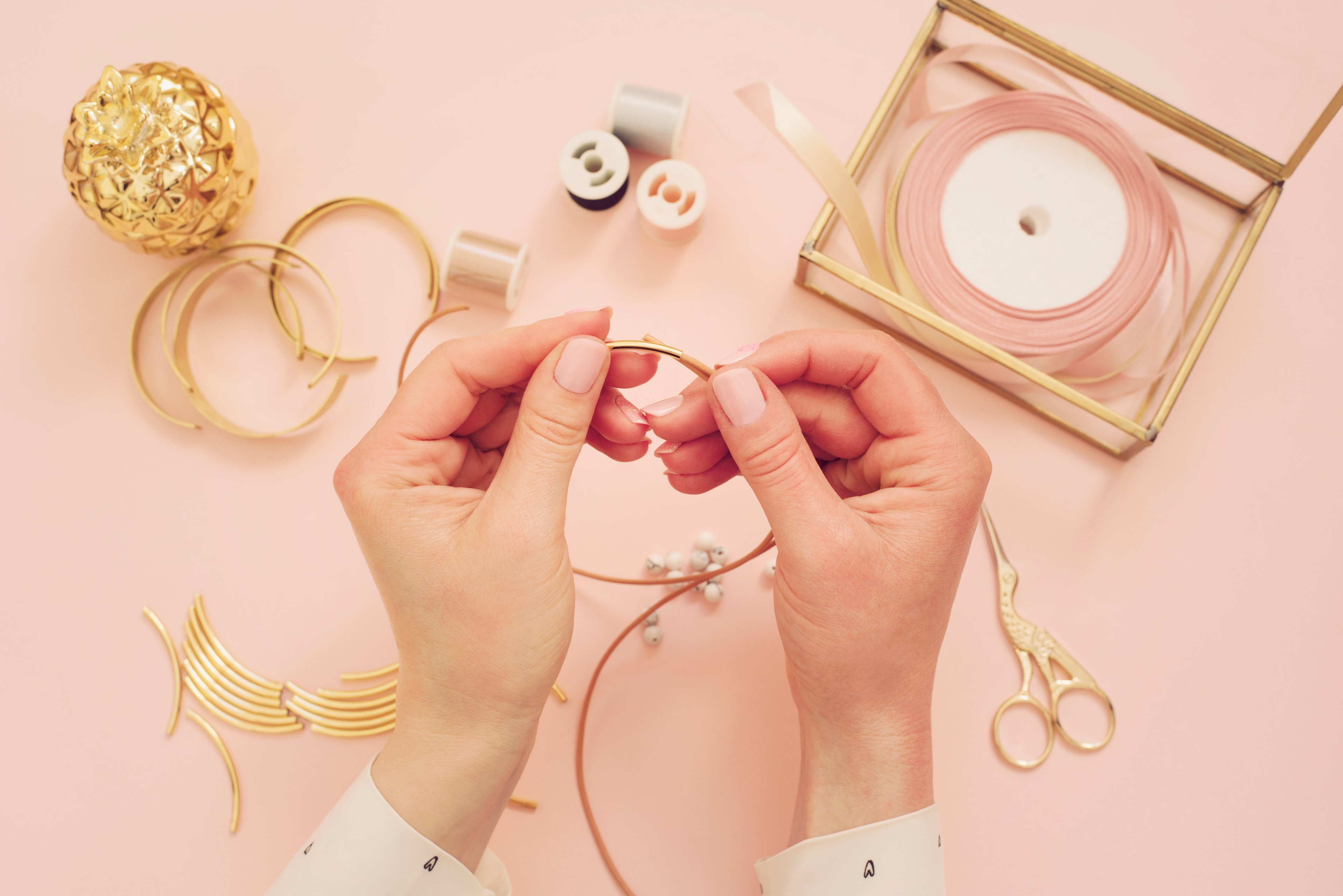 A person crafting using string and wire and scissors on a pink background.