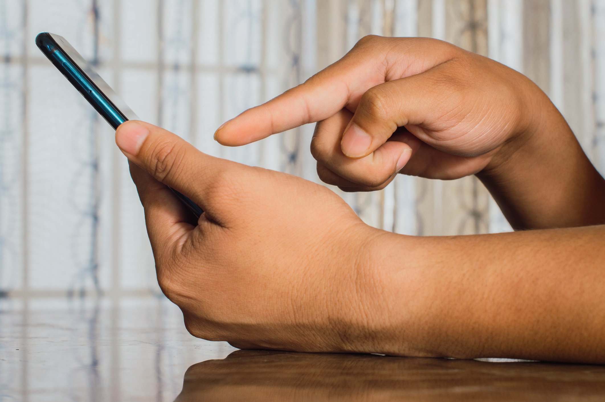 One hand holding a cell phone while the other hand points to the screen.