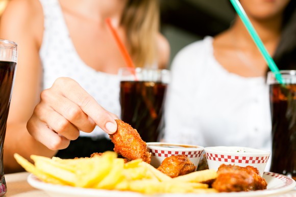 Two women eating chicken wings with sodas.
