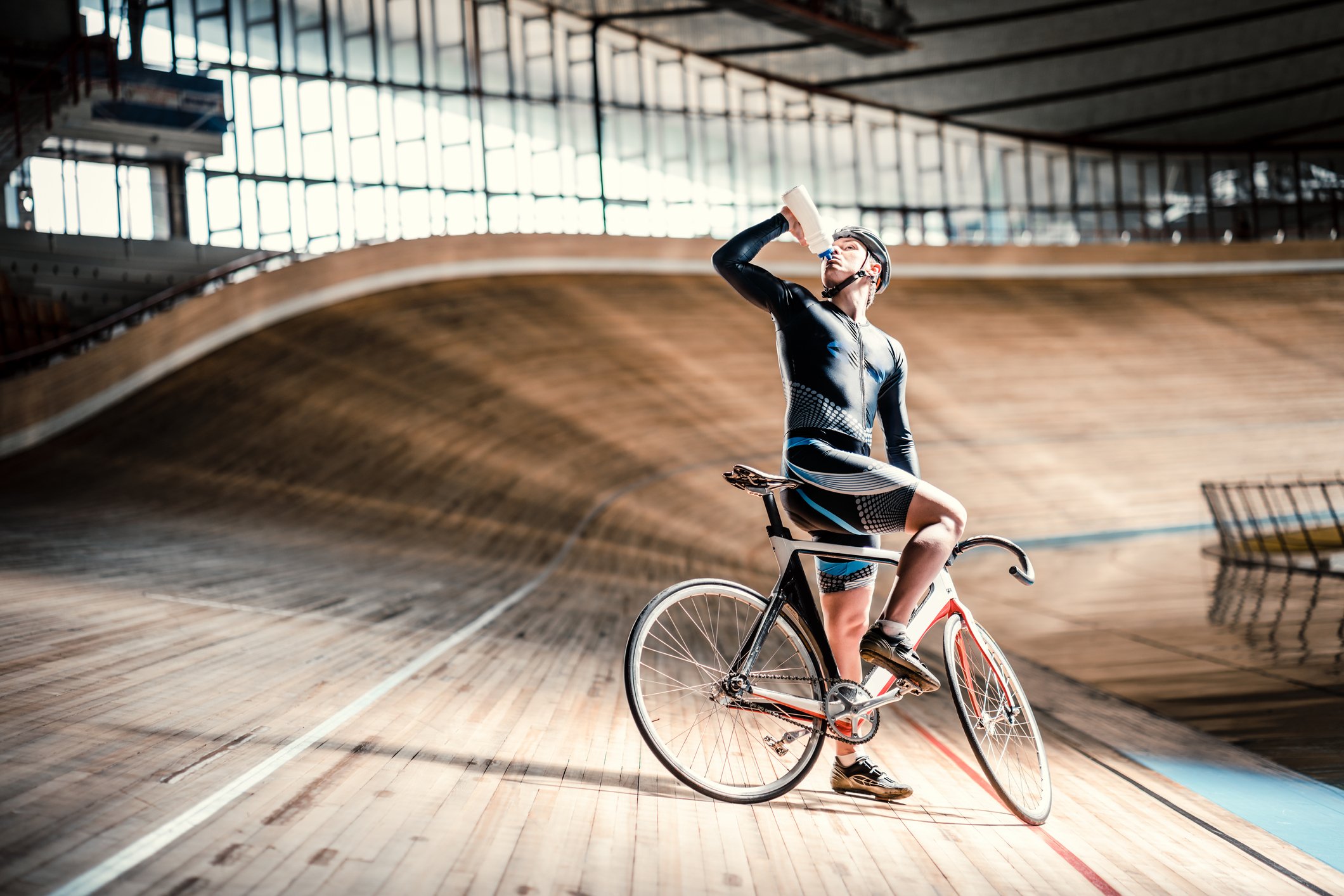 Bicyclist in an indoor track taking a break and taking a drink.
