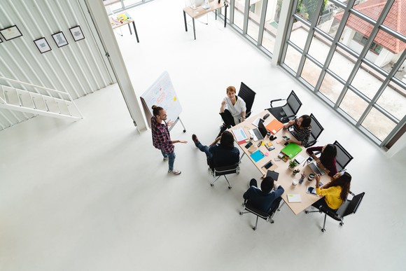 A group of people holds a meeting in a large, airy room, as seen from above.