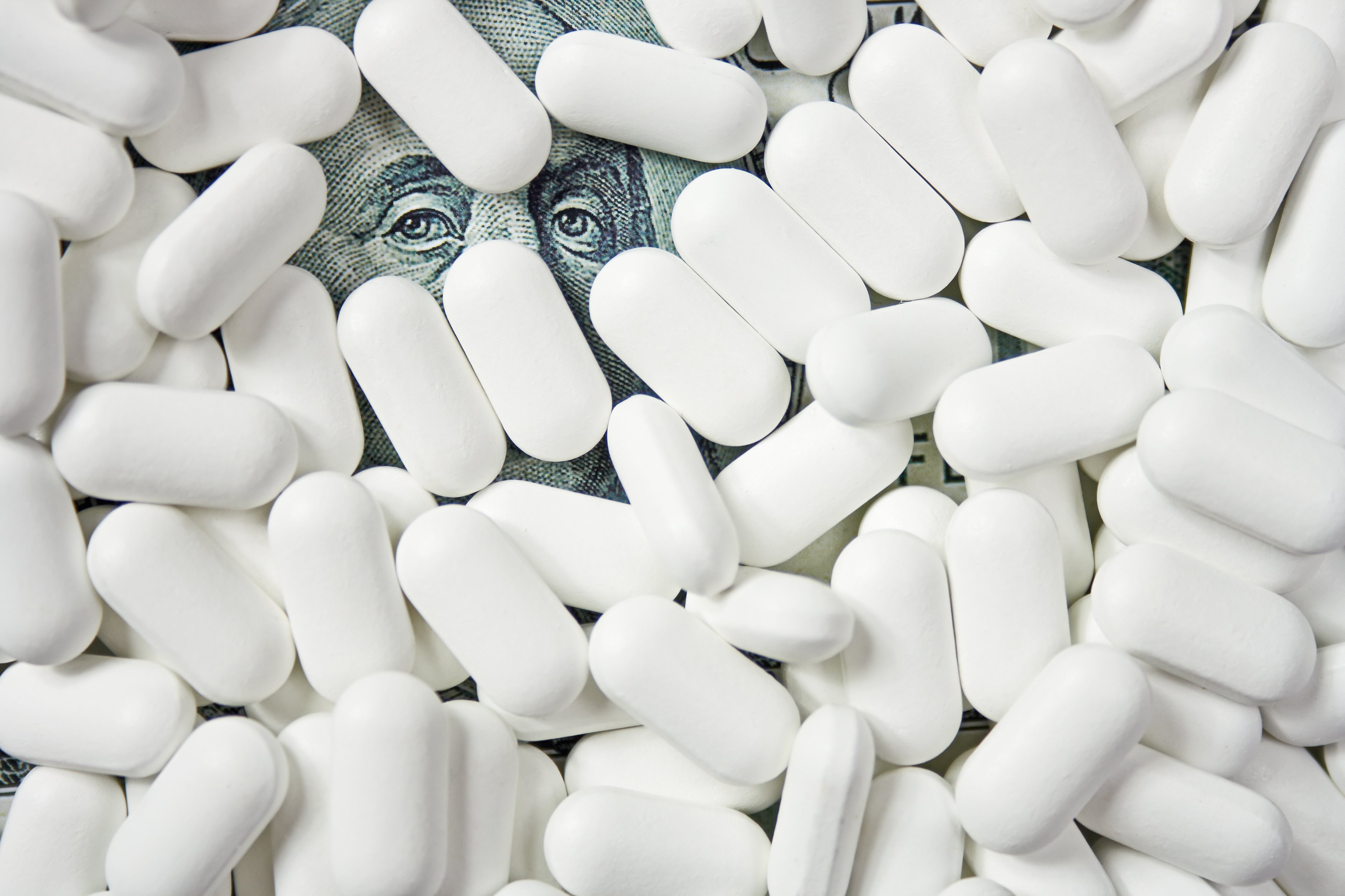 Ben Franklin's face on a hundred-dollar bill peeking out from under white tablets.