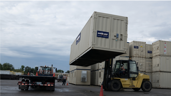 Industrial vehicles moving large storage containers with the Mobile Mini logo on the side.