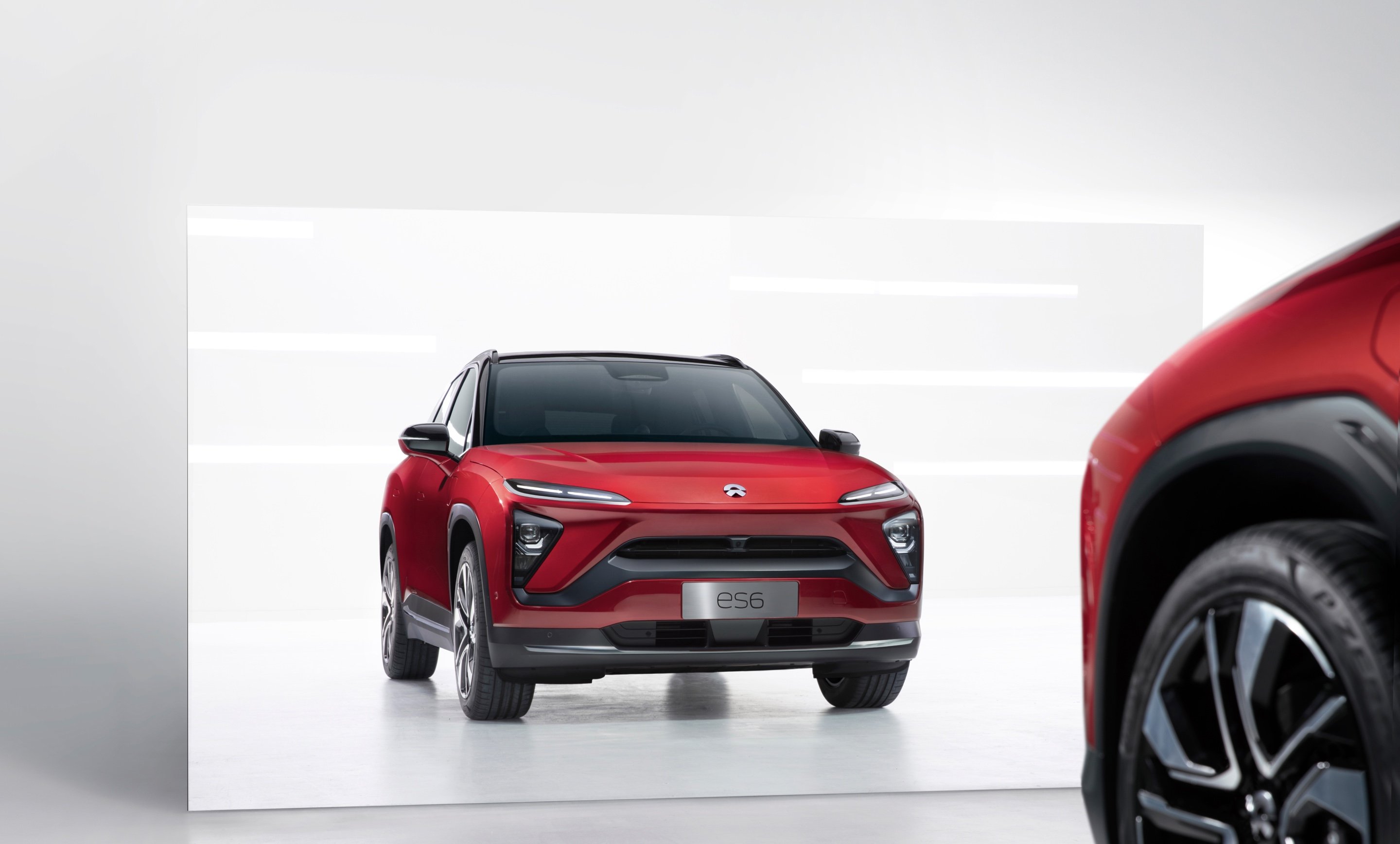 A NIO ES6 SUV in red, pulled up to and reflected in a mirror.