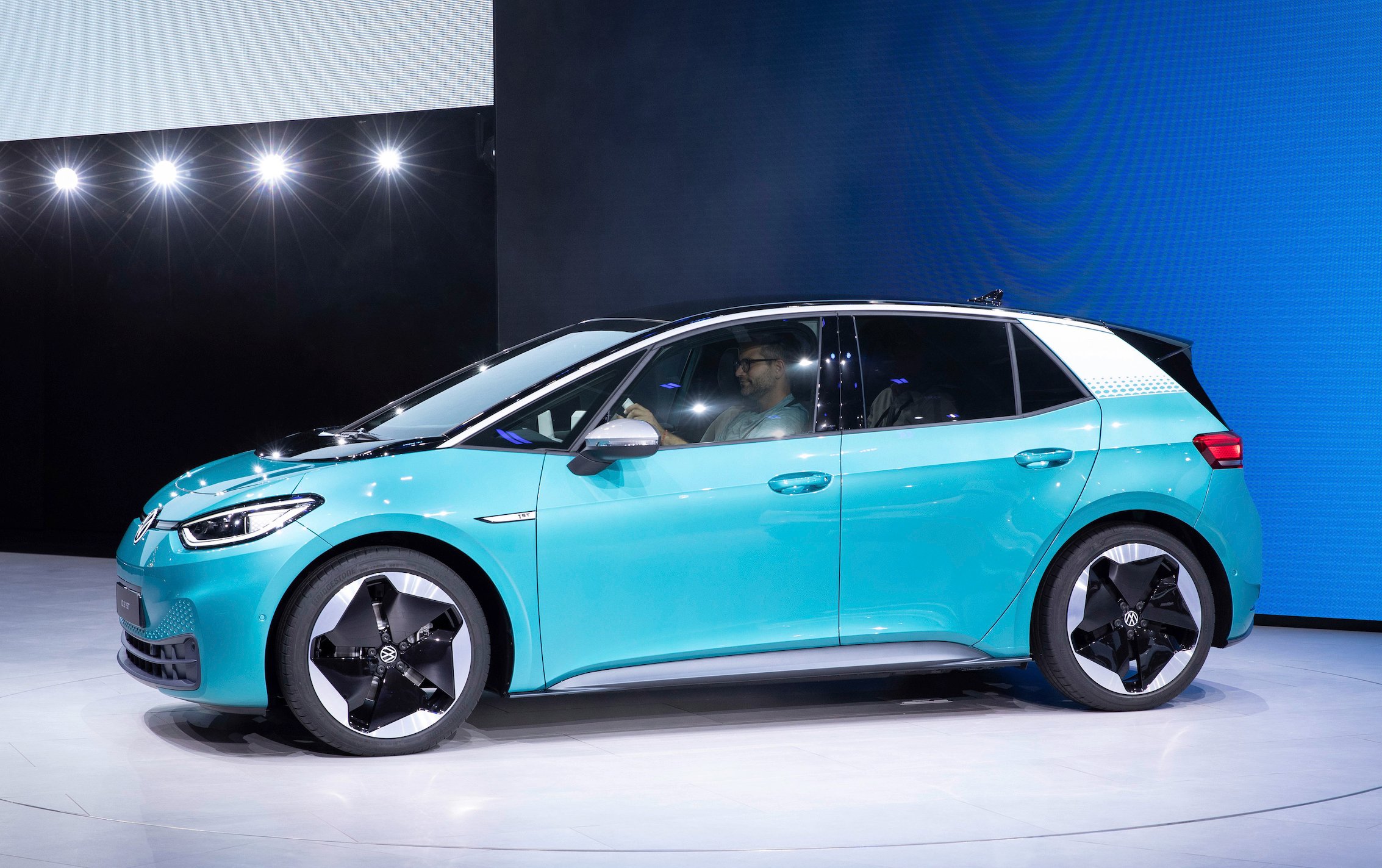 A Volkswagen ID3, a battery-electric hatchback, shown on an auto-show stand.