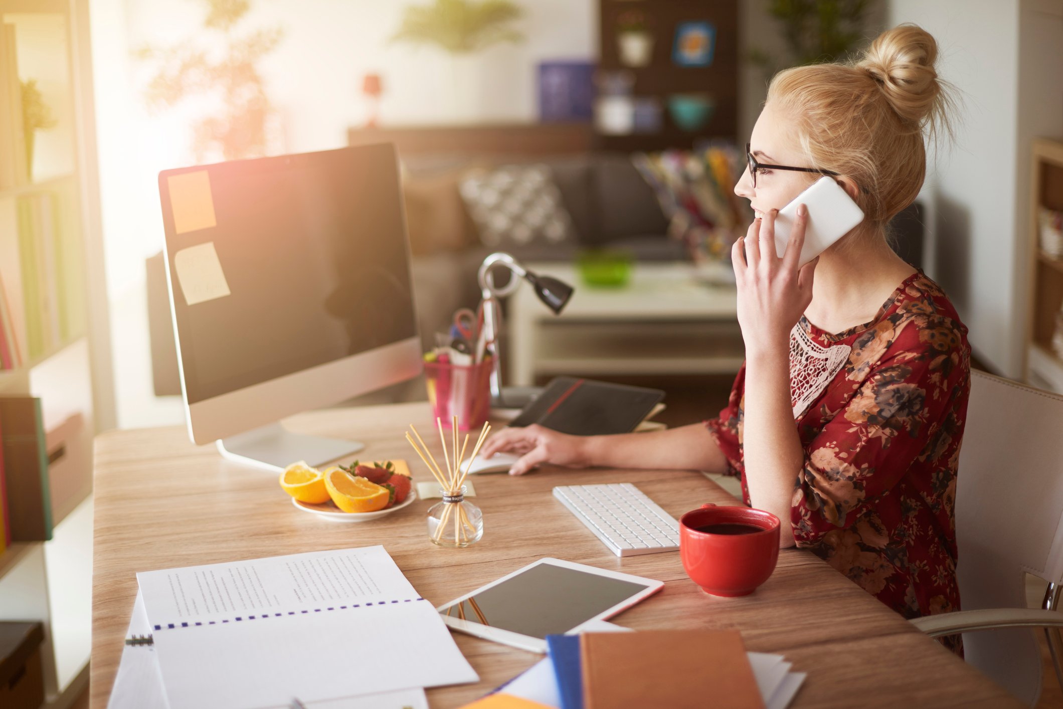 Woman at desk talking on phone, with couch in background.