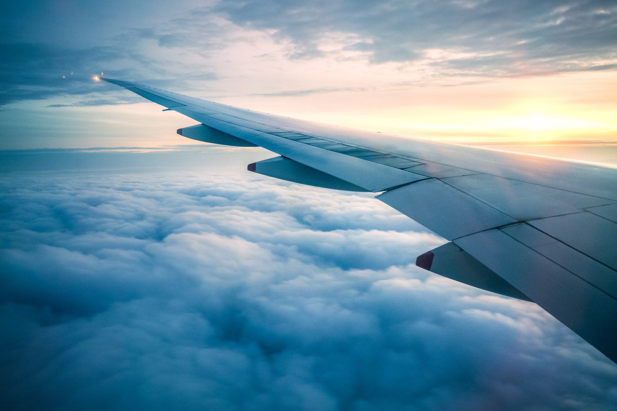 View of an airplane's wing and clouds below at dusk.